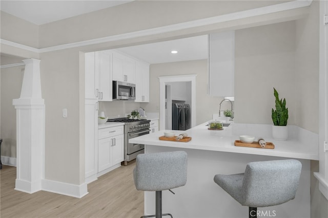 kitchen featuring a breakfast bar, a peninsula, stainless steel appliances, washer and dryer, and a sink