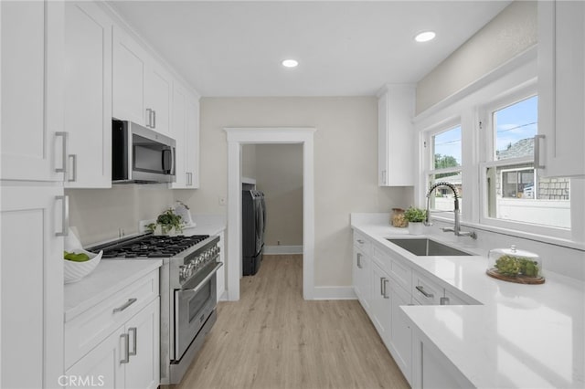 kitchen with stainless steel appliances, a sink, white cabinetry, light countertops, and washer / dryer