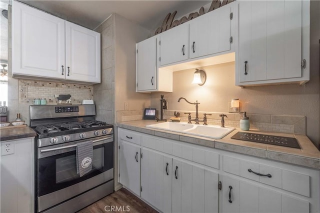 kitchen with stainless steel gas range oven, a sink, white cabinetry, backsplash, and dark wood finished floors