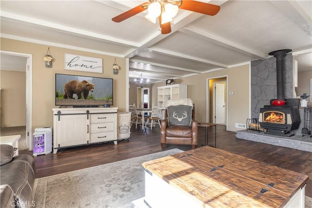 living area with visible vents, beamed ceiling, dark wood finished floors, and a wood stove