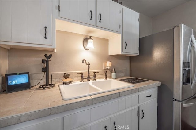 kitchen featuring light countertops, a sink, stainless steel refrigerator with ice dispenser, and white cabinetry