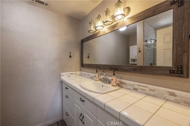 bathroom featuring visible vents, a tile shower, vanity, and baseboards