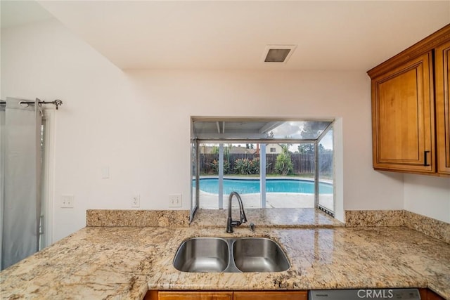 kitchen with dishwashing machine, light stone counters, brown cabinetry, and a sink