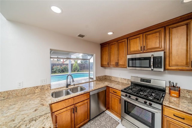 kitchen with appliances with stainless steel finishes, brown cabinetry, a sink, and visible vents