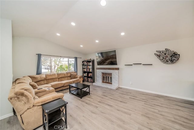 living room with lofted ceiling, recessed lighting, light wood-style floors, a glass covered fireplace, and baseboards