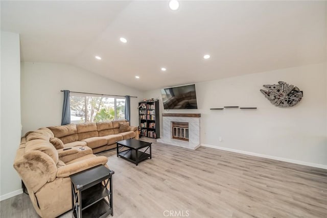 living room with light wood-style flooring, a glass covered fireplace, vaulted ceiling, and recessed lighting