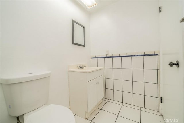 bathroom featuring a wainscoted wall, tile walls, toilet, vanity, and tile patterned floors