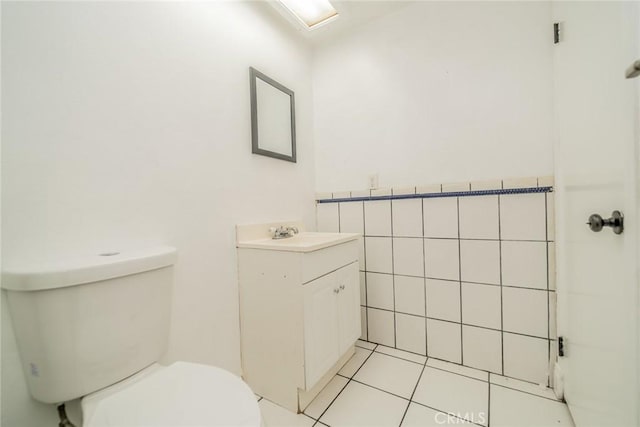 half bathroom with toilet, tile patterned floors, vanity, and tile walls