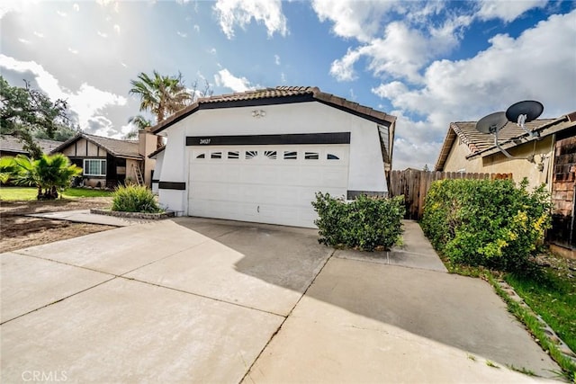 view of front facade featuring stucco siding, fence, a tile roof, an attached garage, and concrete driveway