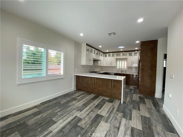 kitchen with visible vents, glass insert cabinets, a peninsula, light countertops, and a sink