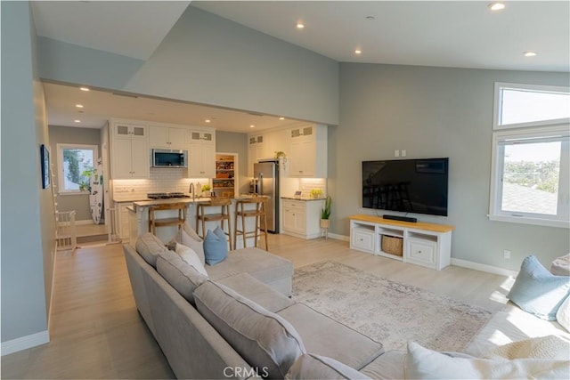 living area featuring high vaulted ceiling, light wood-style flooring, baseboards, and recessed lighting