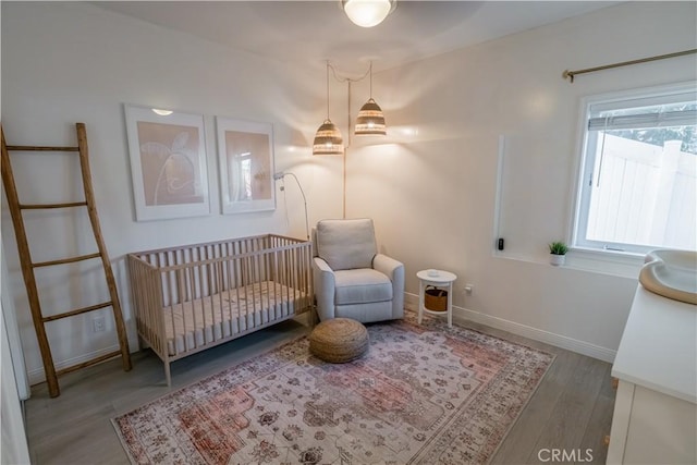 bedroom with a crib, baseboards, and wood finished floors