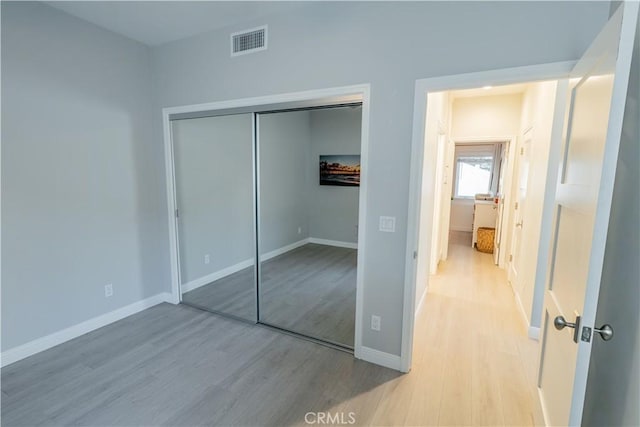 unfurnished bedroom featuring a closet, visible vents, light wood-style flooring, and baseboards