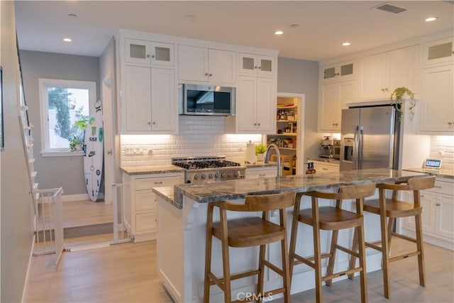 kitchen with appliances with stainless steel finishes, dark stone countertops, visible vents, and white cabinetry