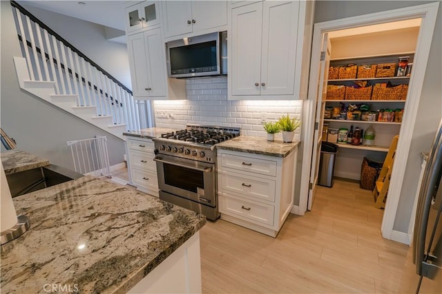 kitchen featuring appliances with stainless steel finishes, light wood-type flooring, white cabinets, and light stone counters