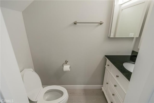 half bathroom with baseboards, vanity, toilet, and wood finished floors