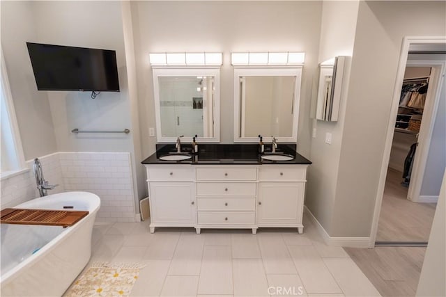 full bathroom featuring a walk in closet, a freestanding tub, a sink, and double vanity