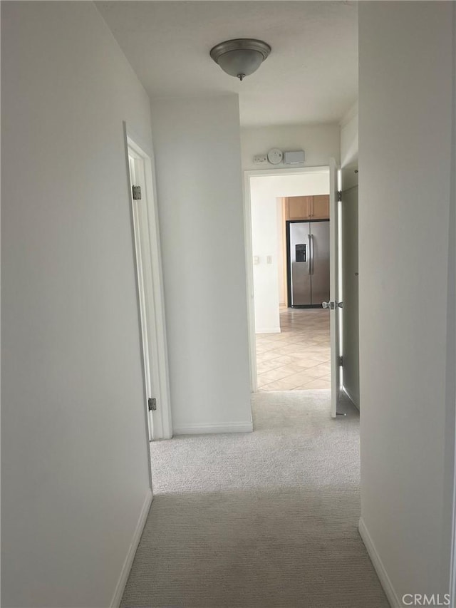 hall with baseboards and light colored carpet