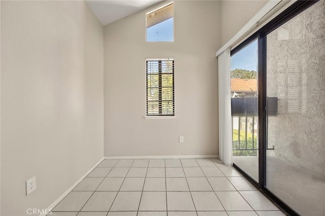 empty room featuring lofted ceiling, light tile patterned floors, and baseboards