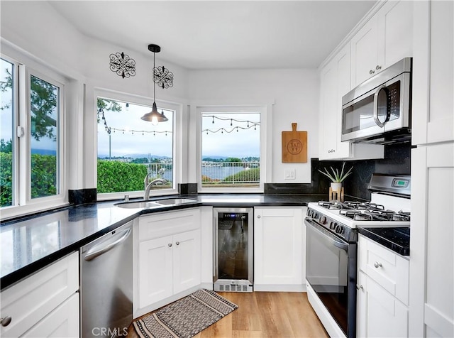 kitchen with wine cooler, a sink, white cabinetry, appliances with stainless steel finishes, and dark countertops