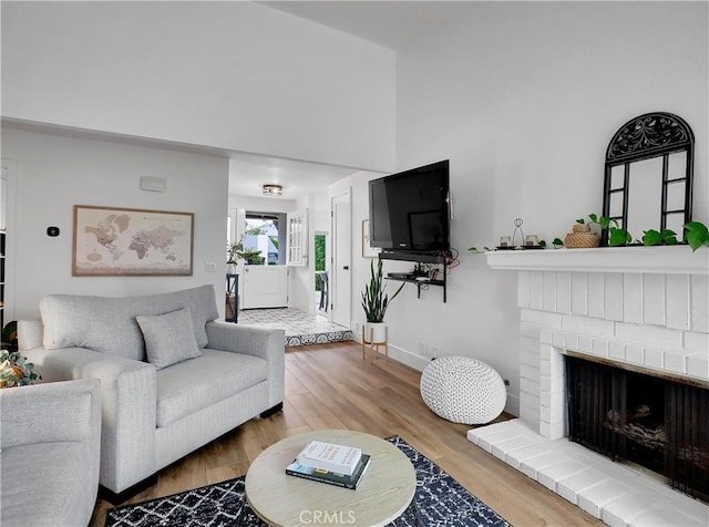 living room featuring a brick fireplace, baseboards, and wood finished floors