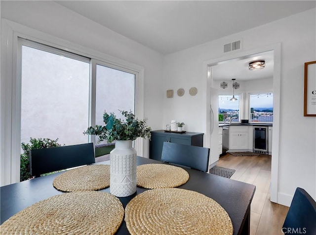 dining space featuring light wood-type flooring, beverage cooler, and visible vents