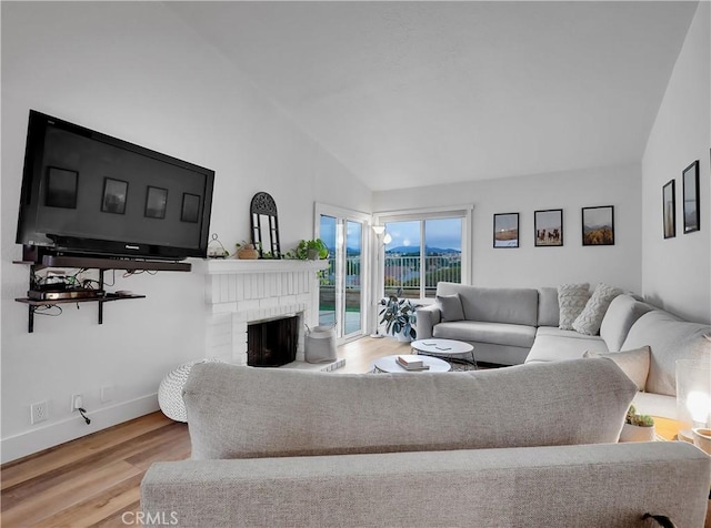 living area featuring a fireplace, baseboards, vaulted ceiling, and wood finished floors