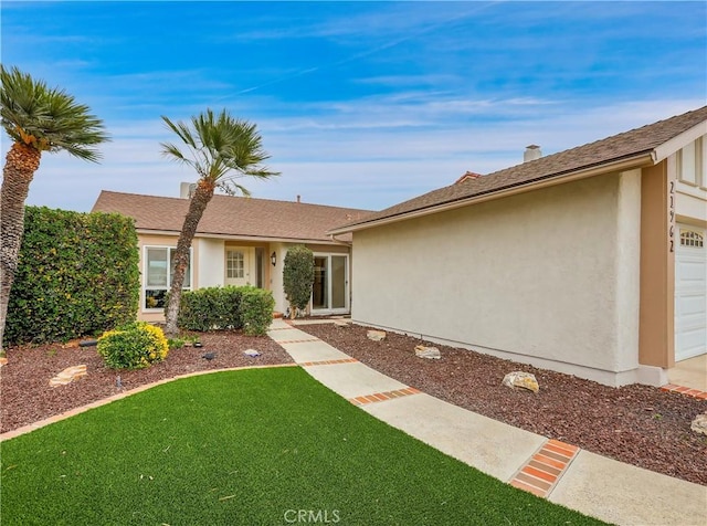 single story home with a garage, a front lawn, and stucco siding