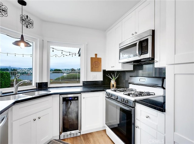 kitchen with dark countertops, wine cooler, stainless steel appliances, white cabinetry, and a sink