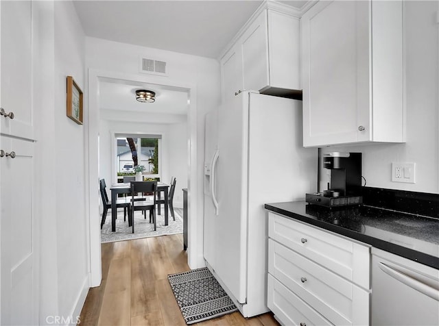 kitchen with white refrigerator with ice dispenser, visible vents, dark countertops, light wood-style floors, and white cabinetry