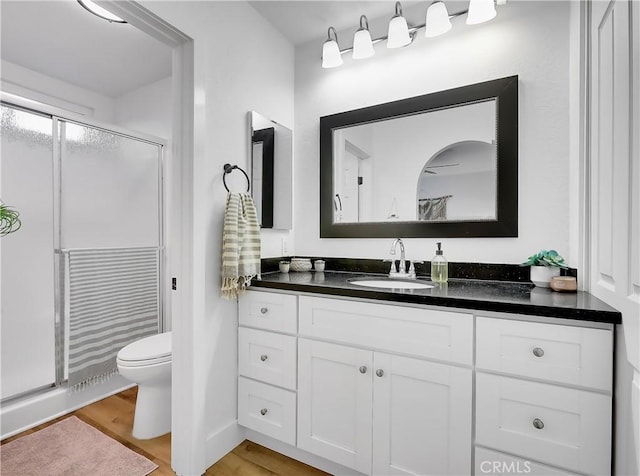 bathroom with toilet, a stall shower, wood finished floors, and vanity