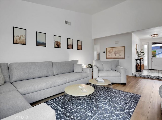 living room with a towering ceiling, visible vents, and wood finished floors