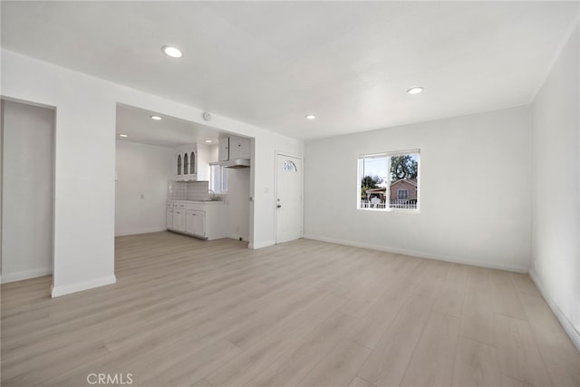 unfurnished living room featuring baseboards, recessed lighting, a sink, and light wood-style floors