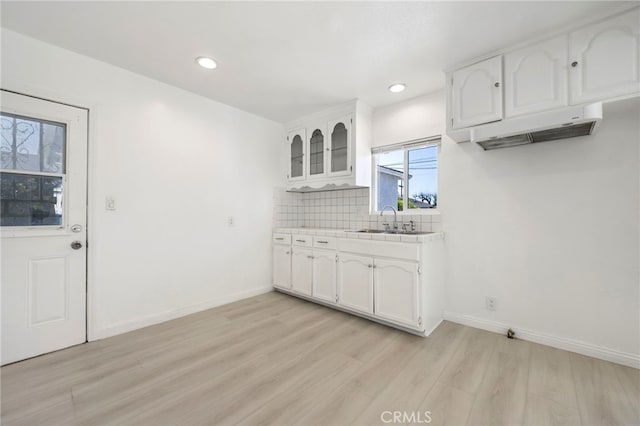 kitchen featuring a sink, white cabinetry, light wood finished floors, glass insert cabinets, and tasteful backsplash