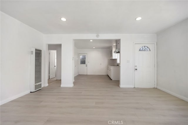 unfurnished living room featuring light wood finished floors, a heating unit, a sink, and baseboards