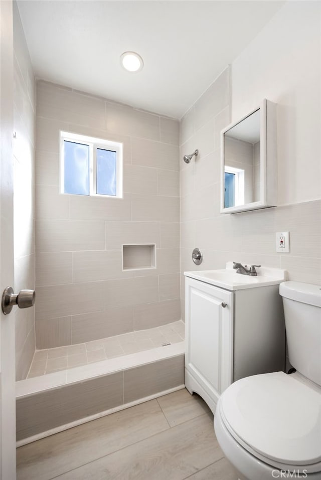 bathroom with tiled shower, vanity, toilet, and wood finished floors