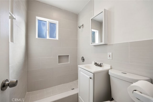 full bath with a tile shower, tile walls, toilet, and vanity