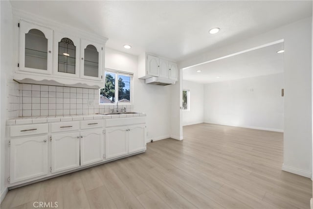 kitchen with light wood finished floors, tasteful backsplash, tile counters, white cabinets, and a sink