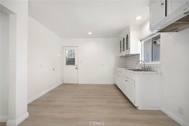 kitchen with light wood finished floors, plenty of natural light, white cabinetry, and backsplash