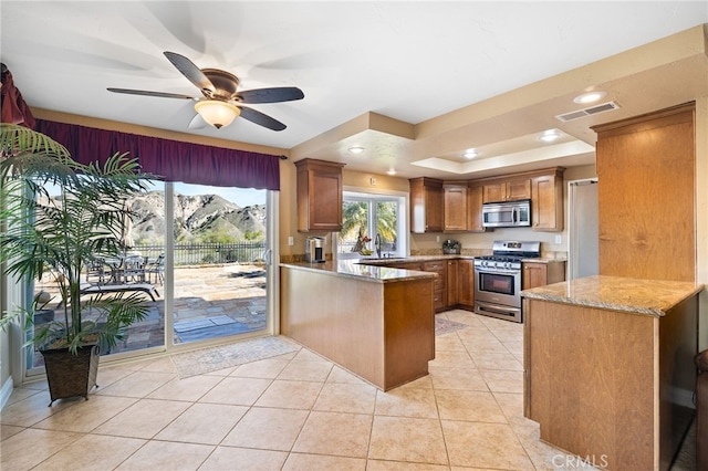 kitchen with visible vents, appliances with stainless steel finishes, a peninsula, brown cabinetry, and light stone countertops