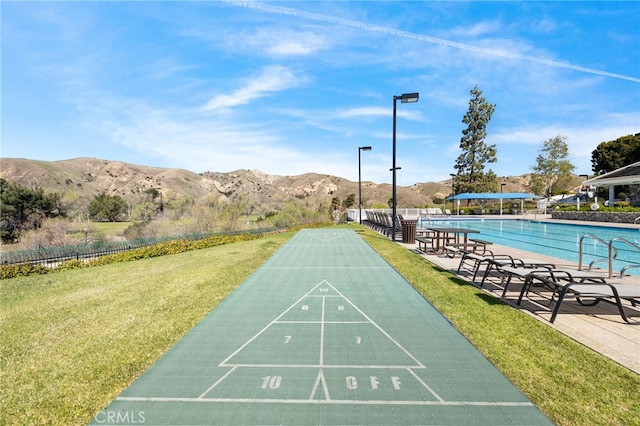 view of home's community with a mountain view, shuffleboard, a lawn, and fence