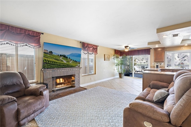 living area featuring baseboards, visible vents, light tile patterned flooring, ceiling fan, and a brick fireplace