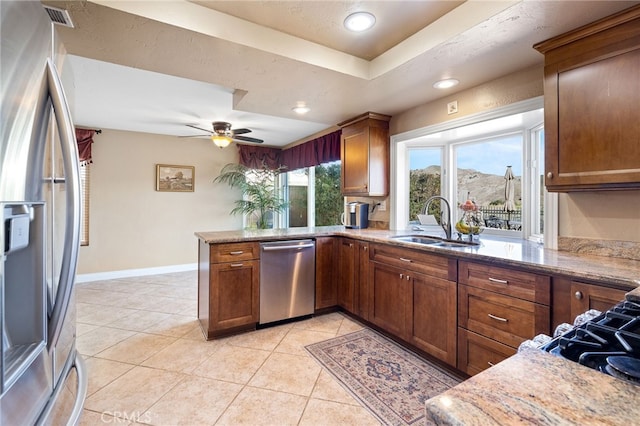 kitchen with light stone countertops, light tile patterned floors, appliances with stainless steel finishes, a peninsula, and a sink