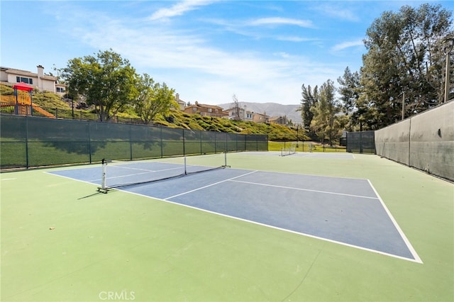 view of tennis court featuring a mountain view, playground community, and fence