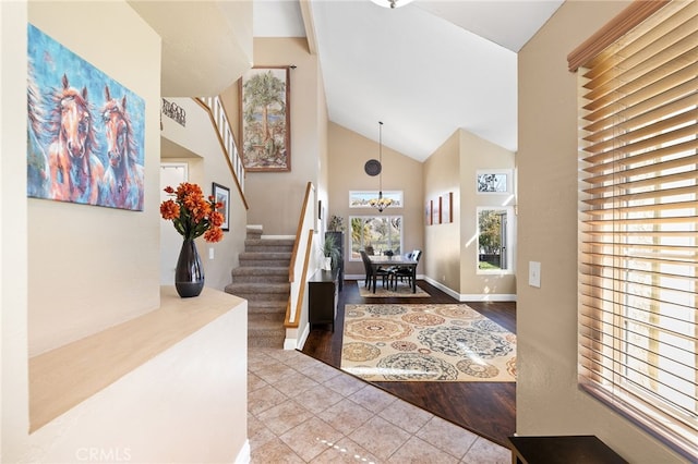 tiled foyer with an inviting chandelier, stairway, baseboards, and high vaulted ceiling