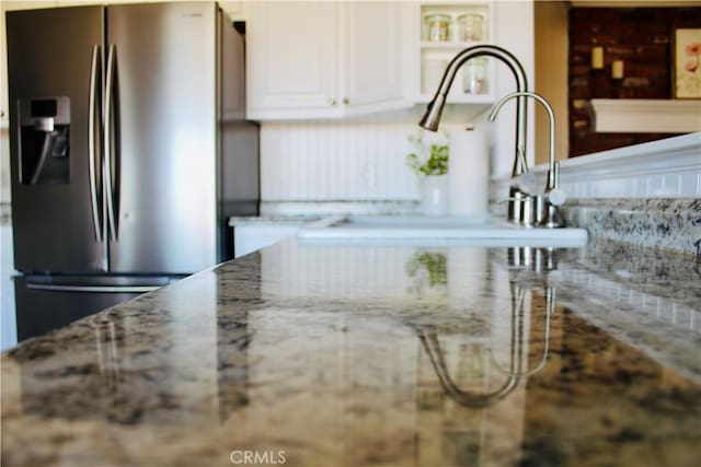 room details featuring light stone counters, white cabinetry, and stainless steel fridge with ice dispenser