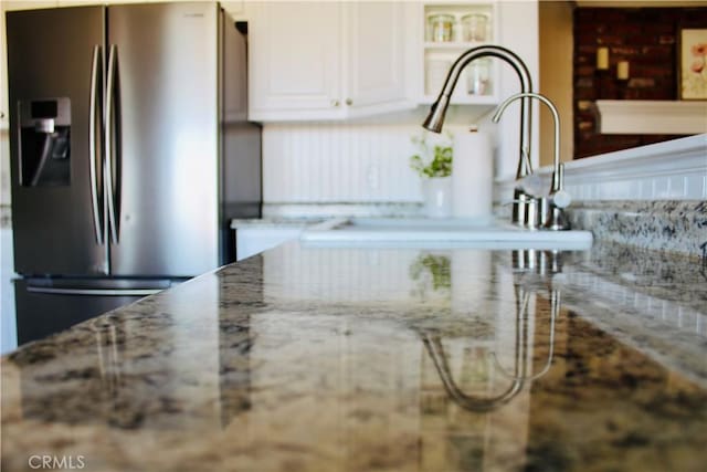 details featuring light stone countertops, white cabinetry, and stainless steel fridge with ice dispenser