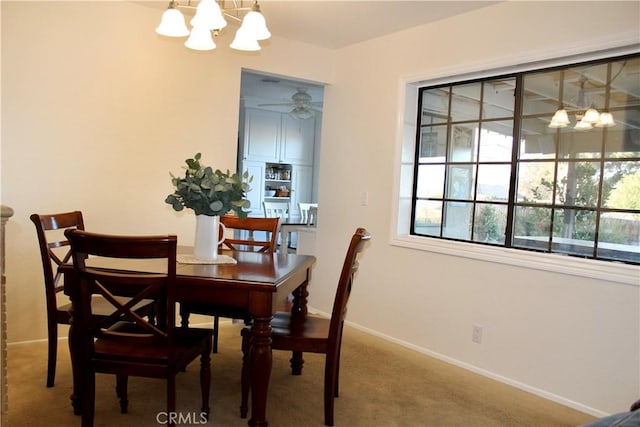 carpeted dining room with ceiling fan with notable chandelier and baseboards