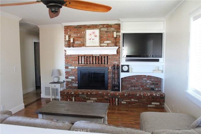 living area with wood finished floors, a ceiling fan, crown molding, baseboards, and a brick fireplace