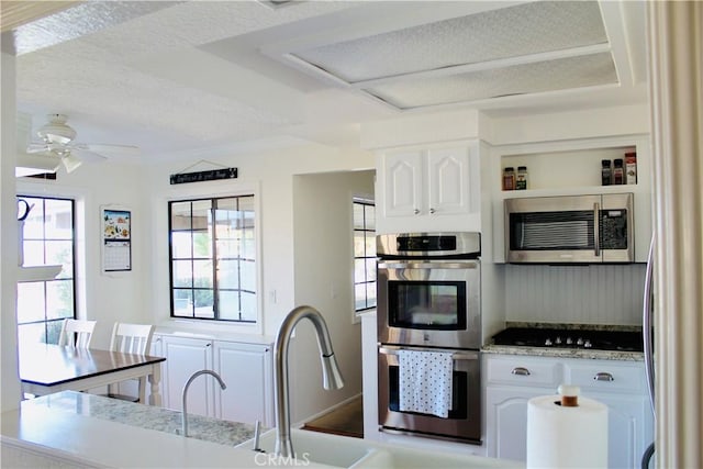 kitchen featuring a textured ceiling, stainless steel appliances, white cabinetry, and a ceiling fan